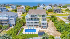 A multi-story residential building with a swimming pool, surrounded by other houses, and a view of the ocean. - New Soundside Dog Friendly Avon Retreat with Pool, Hot Tub, Game Room, Theater (Salvo)