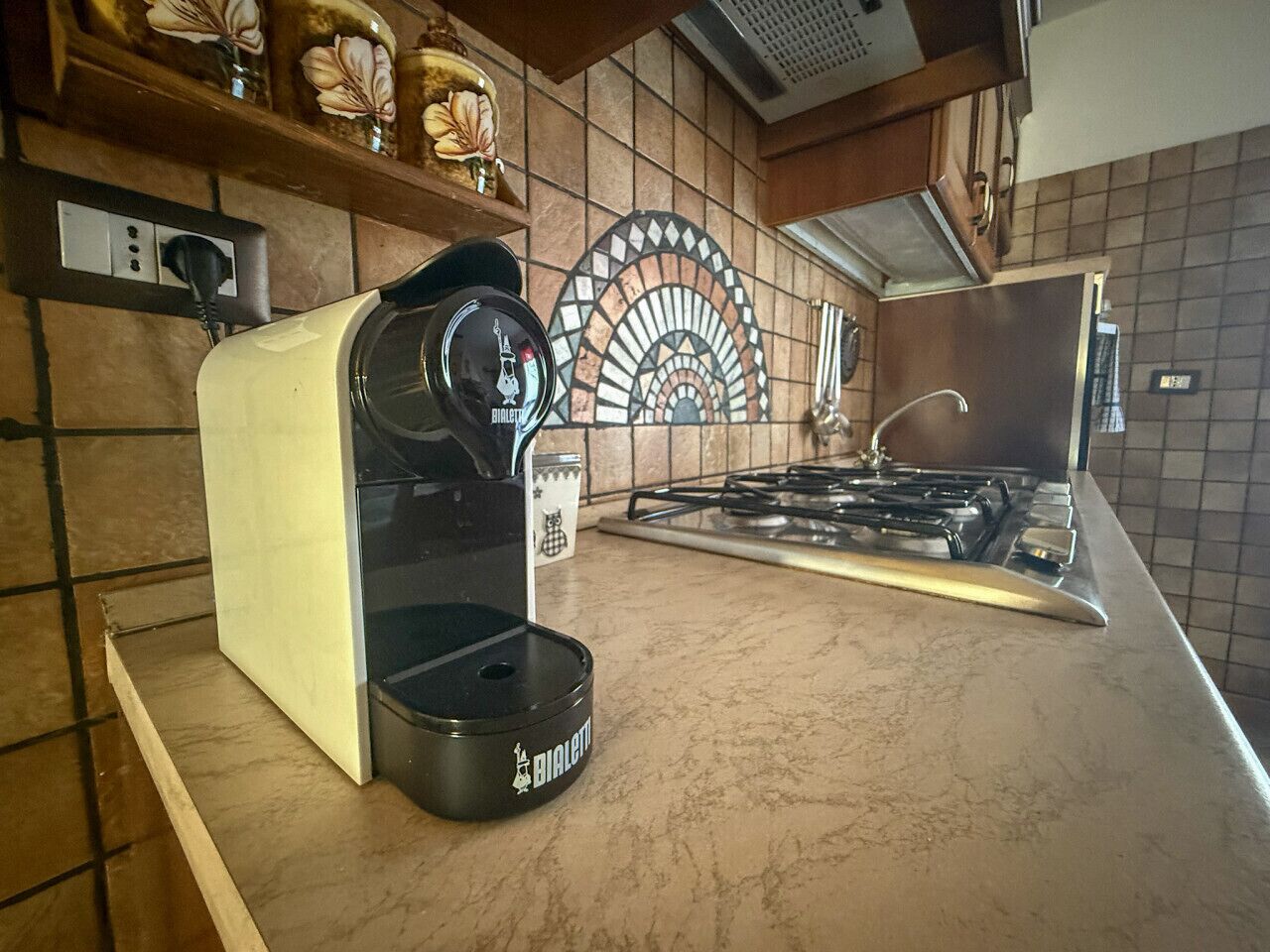 A kitchen with a coffee maker, a stove, and a decorative backsplash.