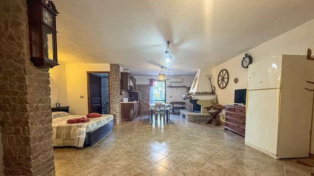 A spacious living area with a dining table, a kitchen area with a refrigerator, and a stone wall. - L`ulivo - Portoscuso (Portoscuso)