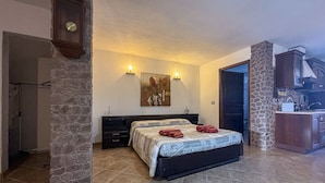 A bedroom with a bed, a stone pillar, a painting, and a kitchen area. - L`ulivo - Portoscuso (Portoscuso)