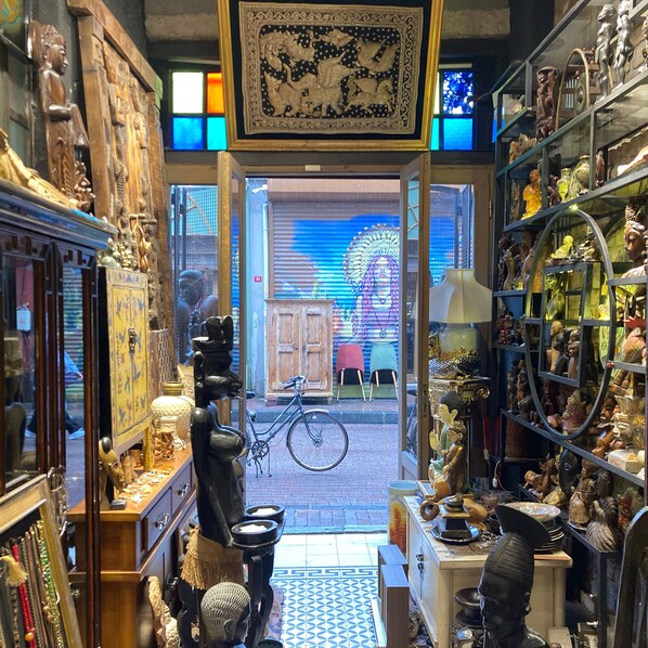 Uma loja estreita com diversas estátuas e artefatos expostos, uma bicicleta no centro, e um grande mural ao fundo.