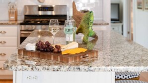 Un piano di lavoro della cucina con ripiano in marmo, un tagliere di legno con formaggio, uva e una bottiglia di vino bianco.