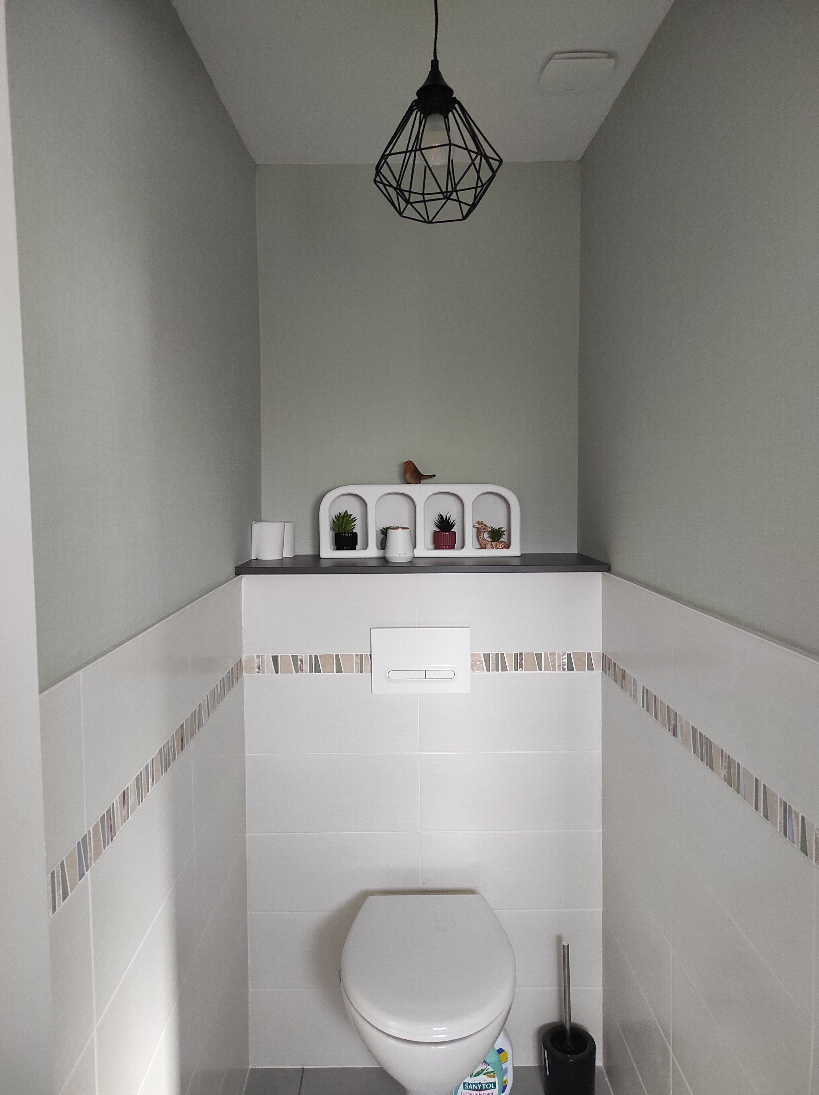 A bathroom with a toilet, a hand dryer, a trash bin, and a hanging light fixture.