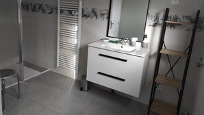 A bathroom with a white vanity, a mirror, a towel rack, a shelf, and a trash bin.