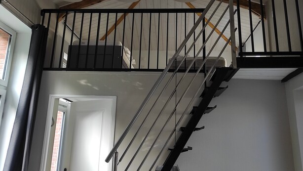 A staircase with a wooden beam ceiling, black railings, and three black pendant lights.