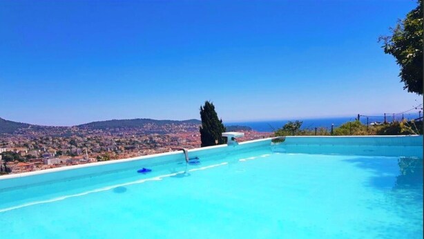 A clear blue infinity pool with a view of a coastal town and the sea. - Villa baie des anges (Nice)