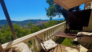 A wooden deck with a white balustrade, cushioned seating, and a piano. - Villa baie des anges (Nice)