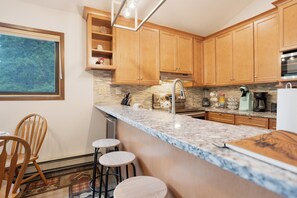A kitchen with wooden cabinets, a granite countertop, and a window with blinds. - Flying Dutchman Slopeside Condo: Pool/Hot Tub Access, On Shuttle Route (Keystone)