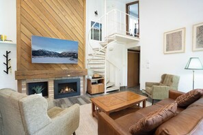 A living room with a fireplace, a wooden wall, a staircase, and a sofa. - Flying Dutchman Slopeside Condo: Pool/Hot Tub Access, On Shuttle Route (Keystone)