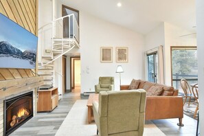 A modern living room with a fireplace, a staircase, a sofa, and a large window. - Flying Dutchman Slopeside Condo: Pool/Hot Tub Access, On Shuttle Route (Keystone)