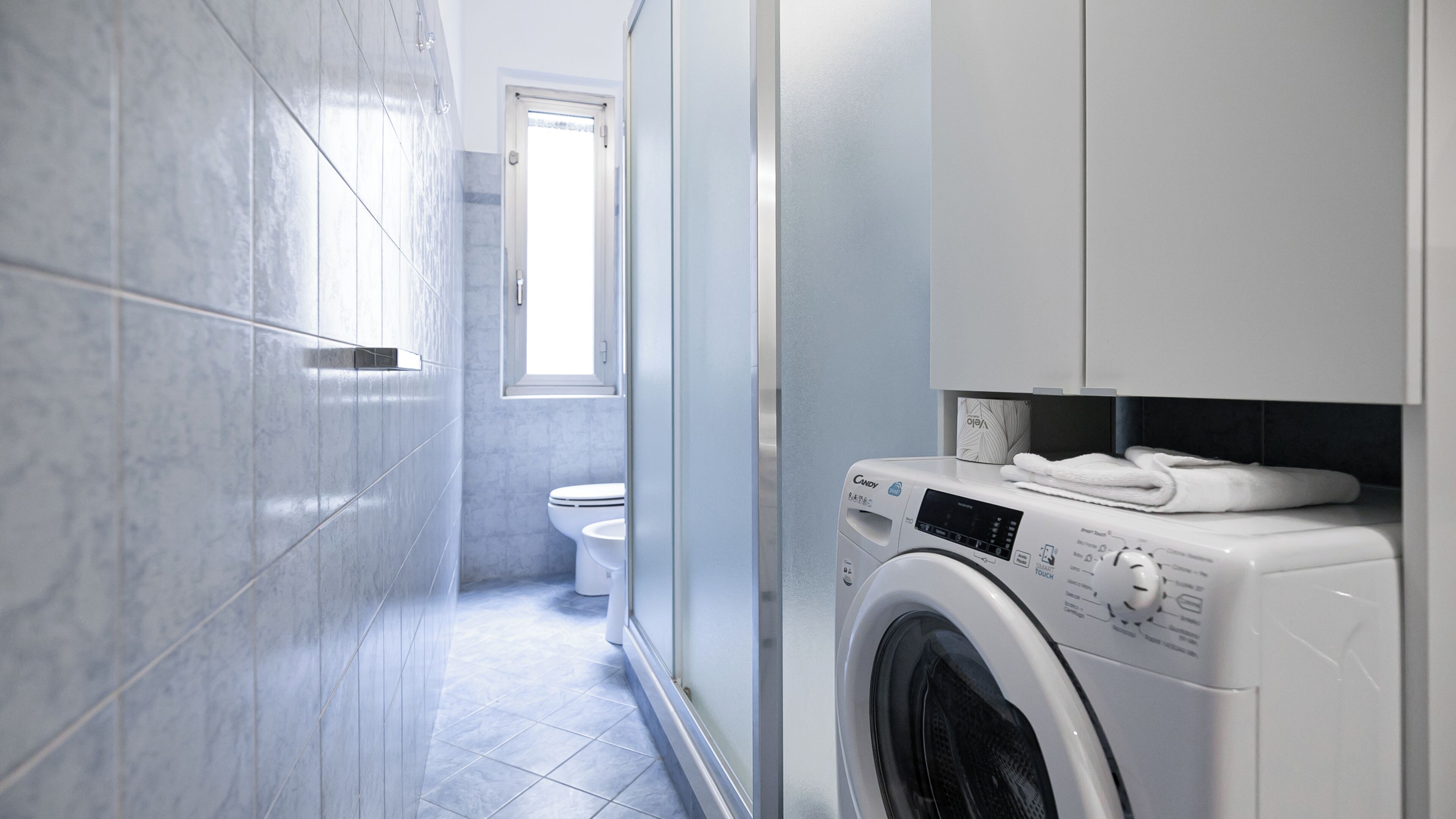 Een moderne badkamer met een wasmachine, toilet en een raam dat voor natuurlijk licht zorgt.