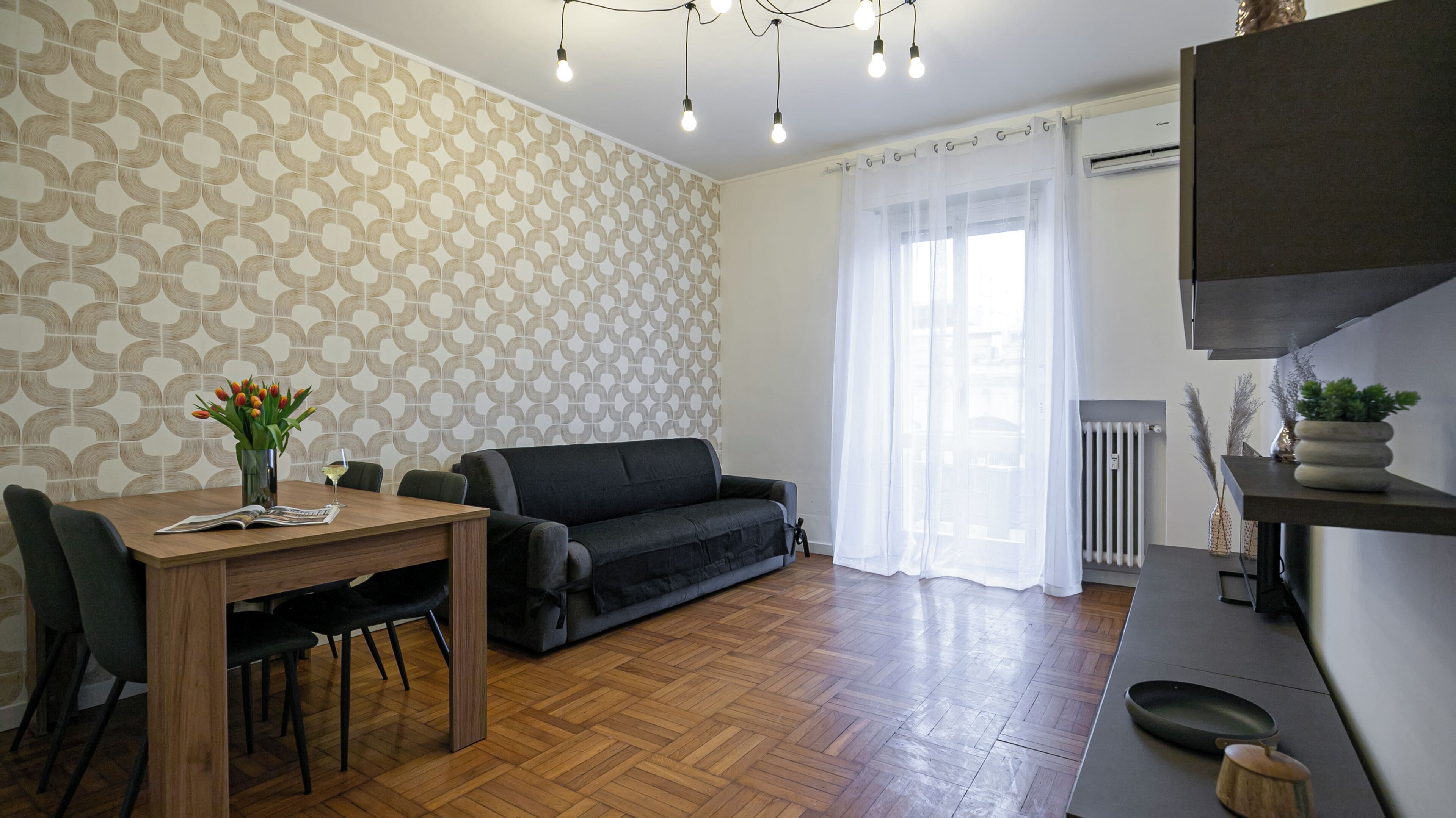 A modern living room with a wooden dining table, black sofa, and patterned wallpaper.