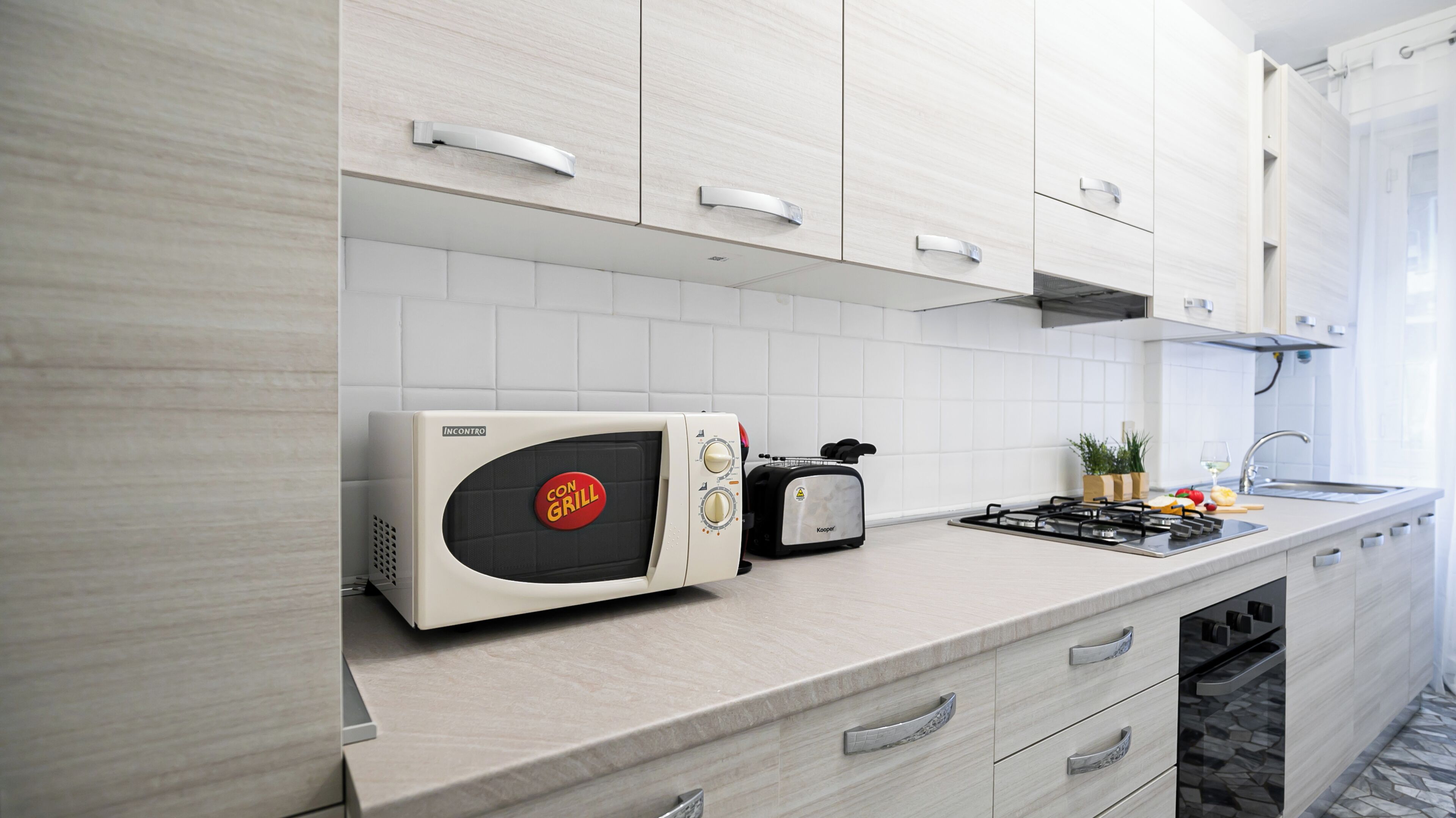 A modern kitchen with white cabinetry, a built-in microwave, a toaster, and a gas stove.