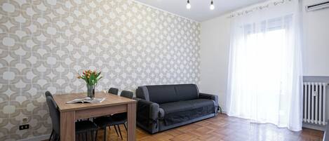 Ein modernes Wohnzimmer mit einem Holzesstisch, schwarzen Stühlen, einem grauen Sofa und Wandtapete mit Muster.