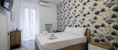A neatly made bed with folded towels, a bedside table with a lamp, and a wall with a floral pattern.