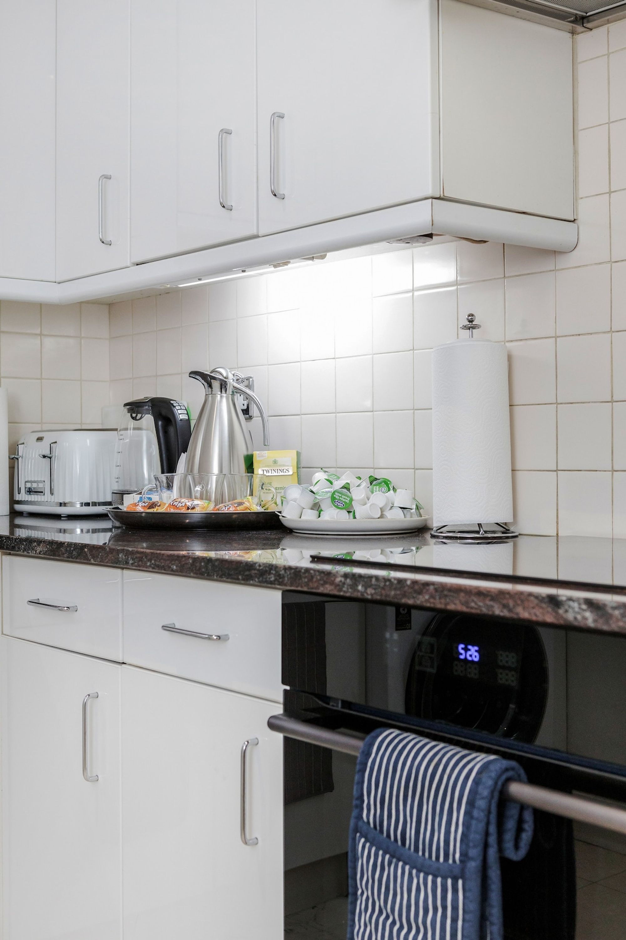 Una cucina con mobili bianchi, una macchina da caffè, un bollitore, un tostapane e un forno a microonde.