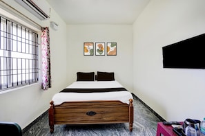 Une chambre d’hôtel bien rangée, avec un lit, une fenêtre grillagée, un climatiseur fixé au mur et un téléviseur à écran plat.