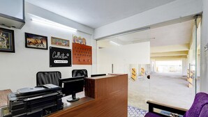 A reception area with a wooden desk, computer, and printer. There are framed pictures on the wall and a calendar. - Super Collection O Sathyabama University (Chennai)