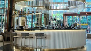 Eine moderne Bar mit einer gebogenen Theke, Barhocker und Blick ins Freie durch große Fenster.
