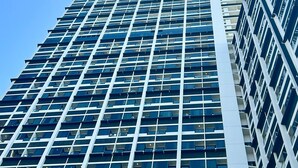 Ein Hochhaus mit einer gitterförmigen Fassade, mehreren Balkonen und blauem Himmel im Hintergrund.
