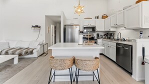 Uma cozinha moderna com armários brancos, uma ilha central e dois banquetes.