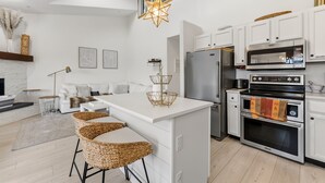 Uma cozinha moderna com armários brancos, uma ilha central, eletrodomésticos de aço inoxidável e uma luminária pendente em formato de estrela.