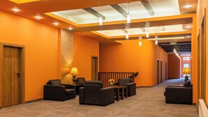 Un vestíbulo de hotel con diseño moderno, que cuenta con una zona de estar central con sofás y sillones, una escalera y un mostrador de recepción.