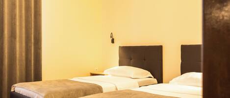 A hotel room with two single beds, a nightstand, a wall-mounted lamp, and a mountain silhouette decoration.