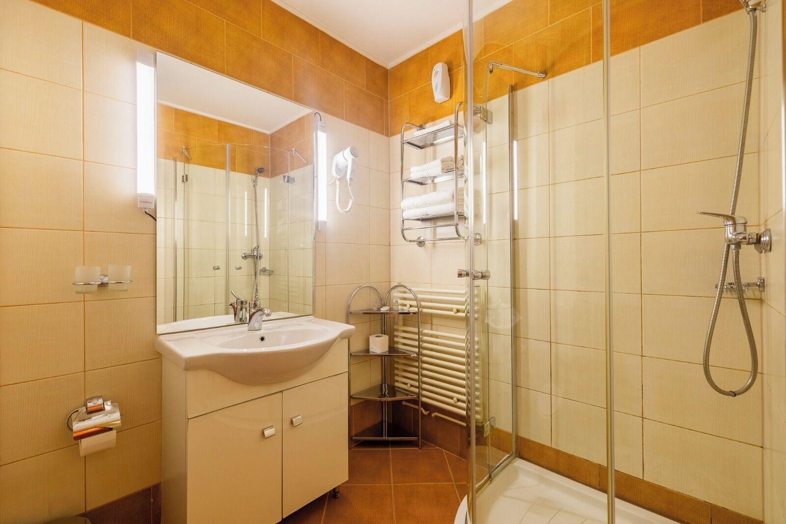 Un baño moderno con lavamanos, espejo, cabina de ducha con mampara de vidrio y toalleros.