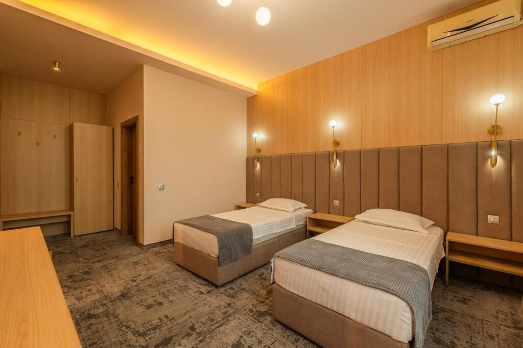A hotel room with two single beds, a wooden wardrobe, a desk, and a bench.