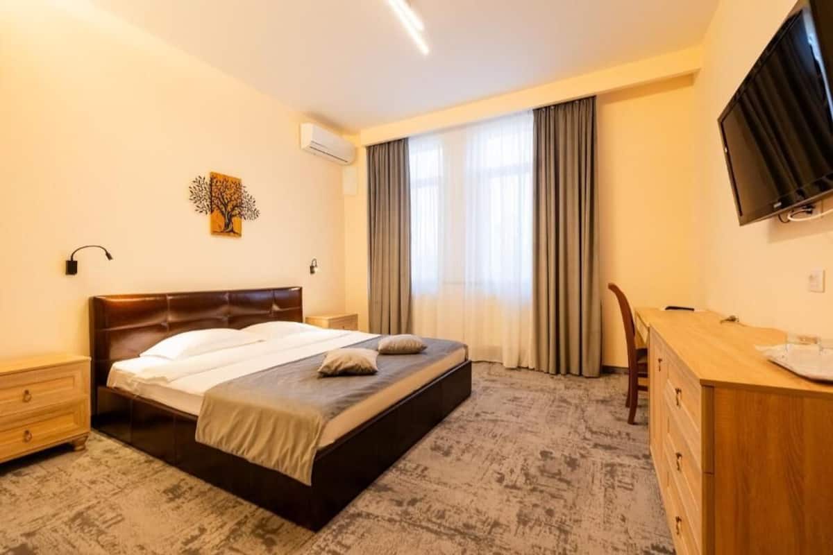 Ett hotellrum med en säng, ett skrivbord, en tv och ett fönster med gardiner.