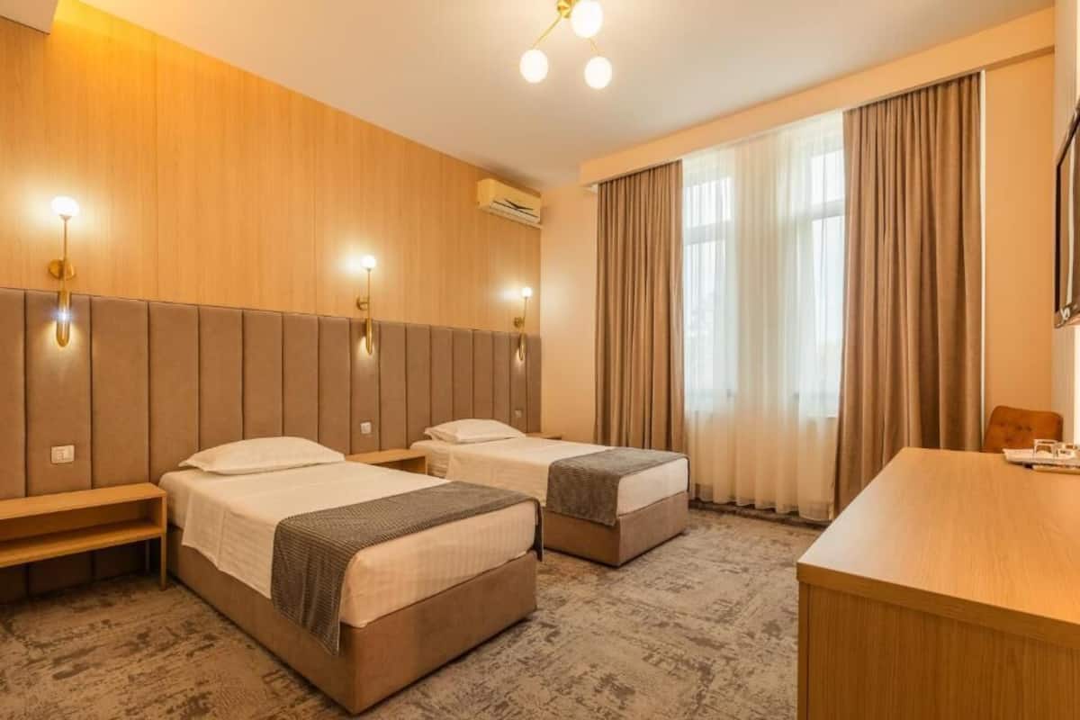 Ett hotellrum med två sängar, ett skrivbord och ett stort fönster med gardiner.
