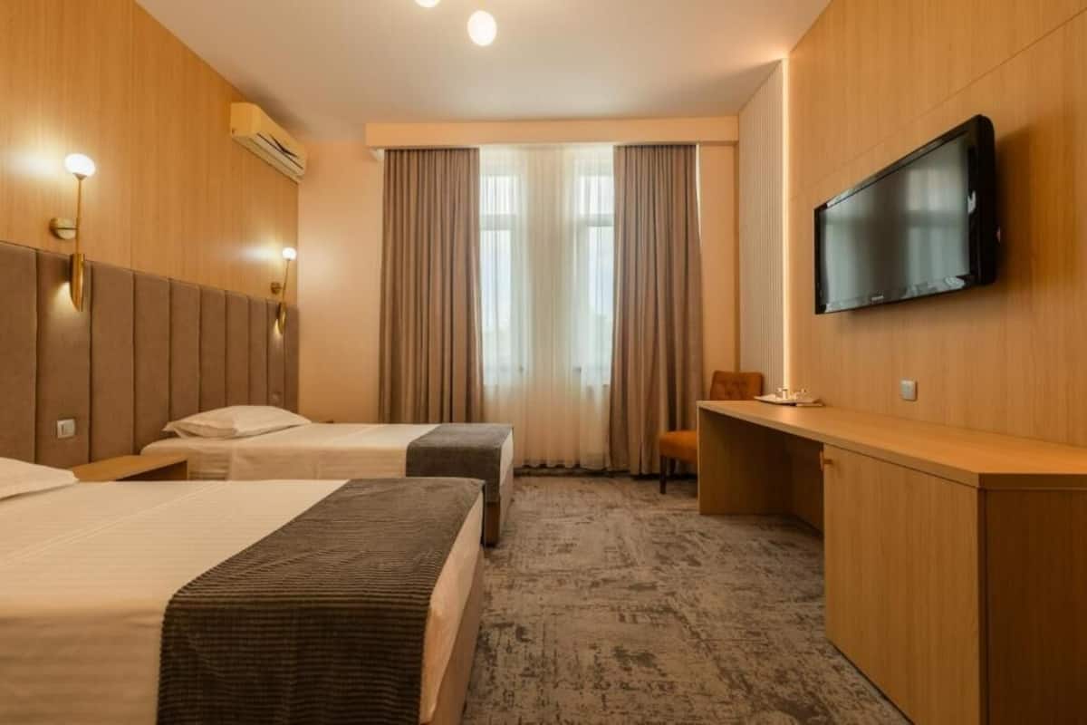 Ett hotellrum med två sängar, ett skrivbord, en tv och ett fönster med gardiner.