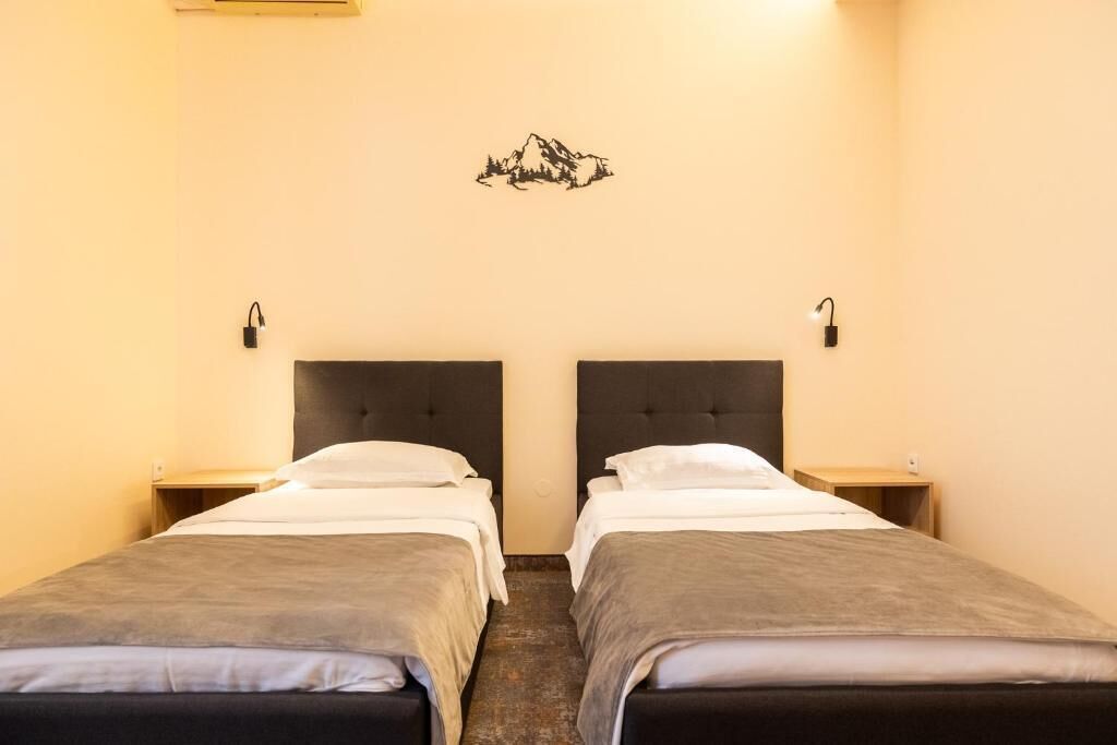 A hotel room with two single beds, a headboard, bedside tables, and a wall-mounted light fixture.