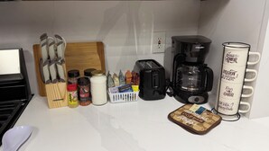 Uma bancada de cozinha com torradeira, cafeteira, prateleira para temperos e suporte para canecas.