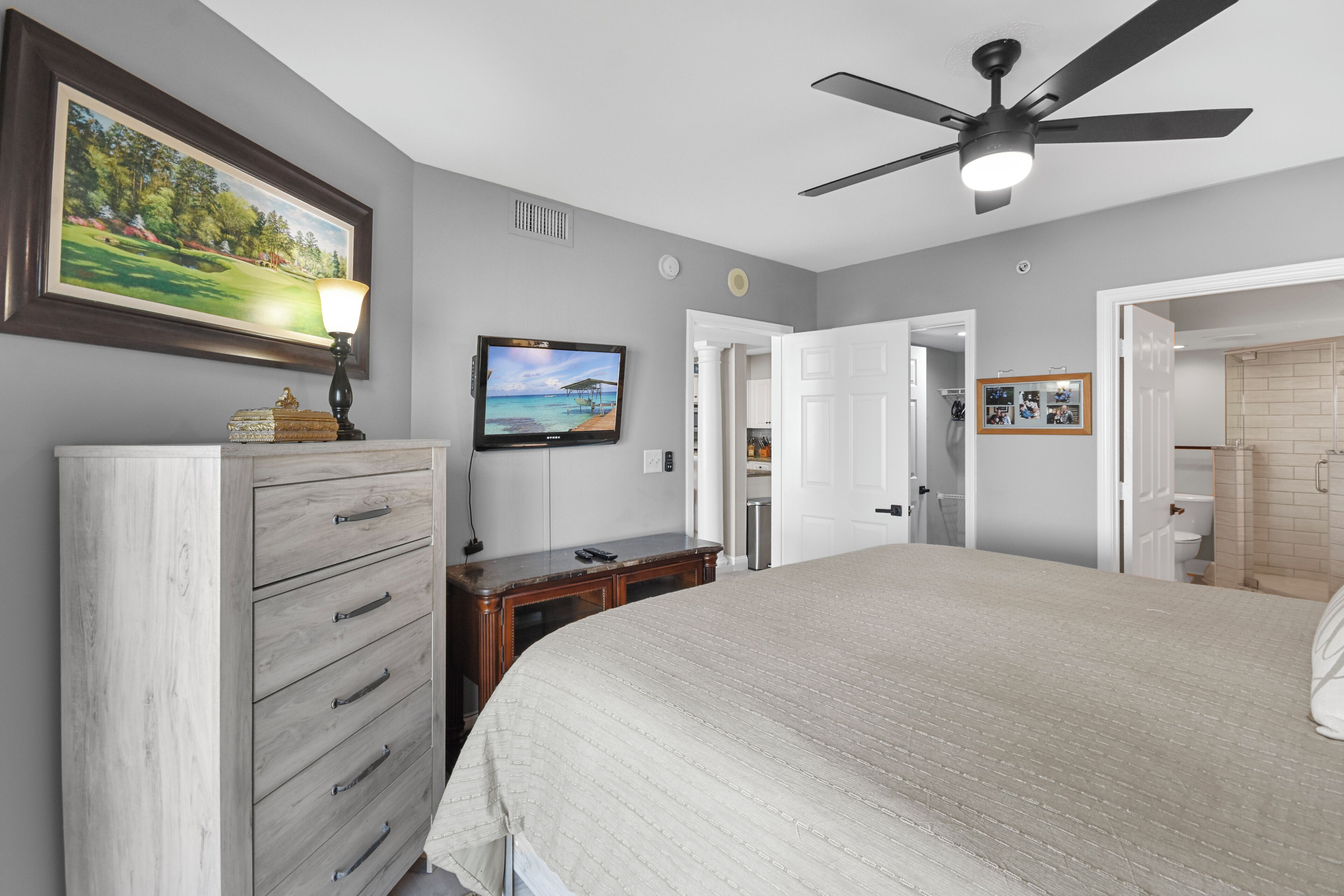 A bedroom with a bed, a dresser, a television, and a ceiling fan.