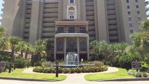 Een groot hotel met een centrale fontein, omringd door verzorgde tuinen en palmbomen.