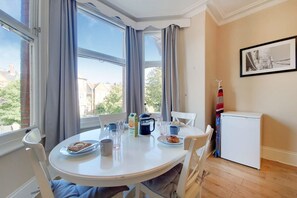 A dining area with a round table, chairs, a small refrigerator, and a window with curtains. - Apartment w Workspace in Ealing (London)