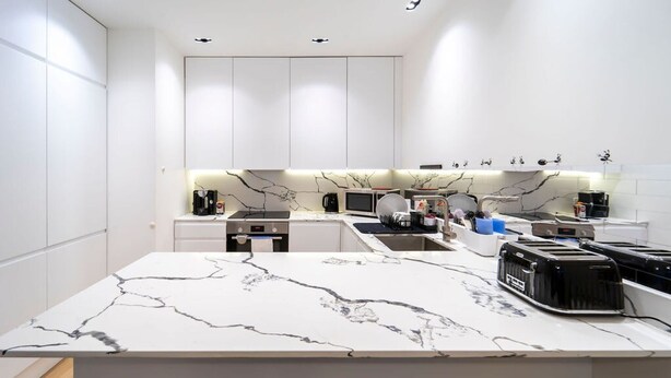 A modern kitchen with white cabinetry, a marble countertop, and various appliances. - Modern Duplex in Ealing Common (London)