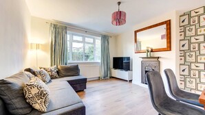 A modern living room with a sofa, a TV, a fireplace, and a dining area with chairs. - Modern Flat Near Pitshanger Park (London)