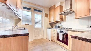 A modern kitchen with wooden cabinets, a built-in oven, and a granite countertop. - Modern Flat Near Pitshanger Park (London)