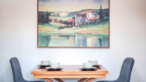 A dining table with four bowls and plates, a painting of a landscape with a building and trees, and a chair. - Modern Flat Near Pitshanger Park (London)