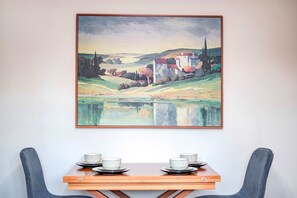 A dining table with four bowls and plates, a painting of a landscape with a building and trees, and a chair. - Modern Flat Near Pitshanger Park (London)