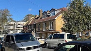 A street view with parked cars, residential buildings, and a clear blue sky. - Quiet Top-floor Retreat (London)