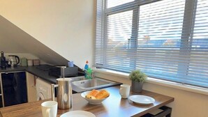 A modern kitchen with a dining area, featuring a wooden table, bar stools, and a window with blinds. - Quiet Top-floor Retreat (London)