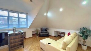 A modern loft apartment with a high ceiling, a large window, a white sofa, a TV, and a small dining area. - Quiet Top-floor Retreat (London)