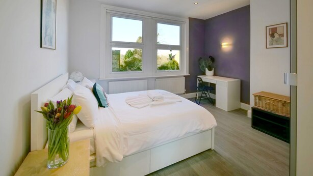A modern bedroom with a large bed, a desk, and a window with a view of greenery. - Apt w Garden Oasis in Finchley (London)