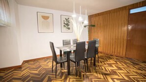 A dining area with a herringbone-patterned floor, a glass-top table, and black chairs.