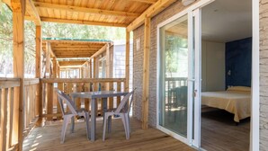 A wooden deck with a table and chairs, leading to a room with a bed and a view of the outdoors. - Hotiday Montalto Marina (Montalto di Castro)