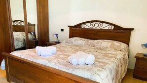 A wooden bed with a patterned bedspread, a nightstand with a lamp, and a mirror on the wall. - The Terrace on the Gulf of Alghero 2 (Alghero)
